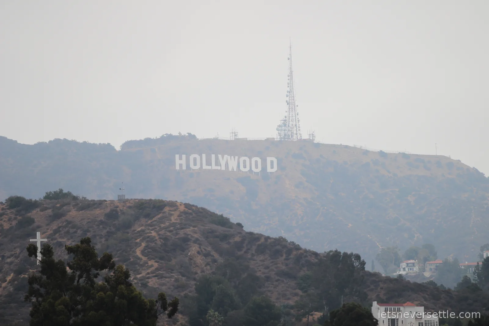 The white letters of the Hollywood Sign on a scrubby hillside through haze