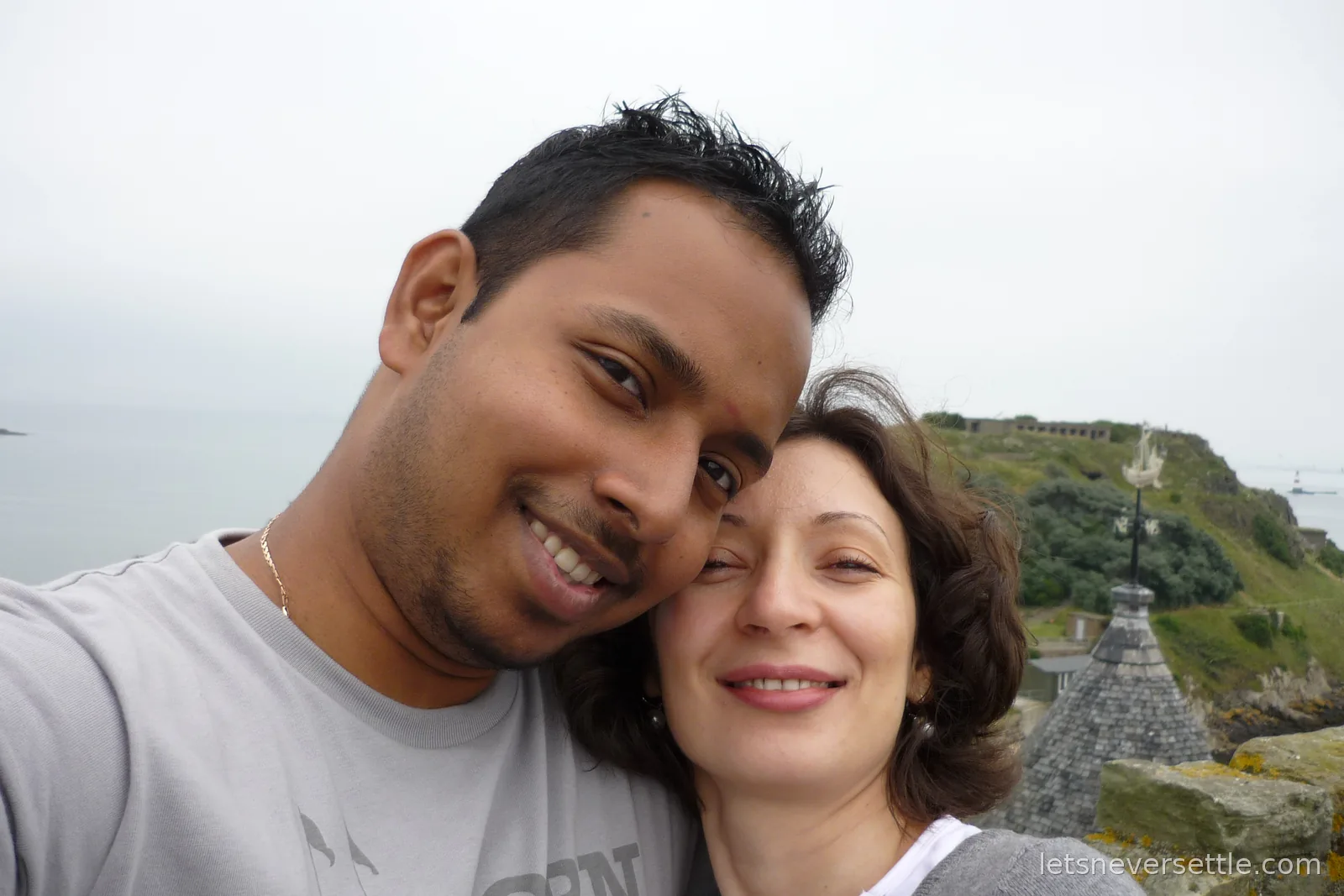 Selfie of Dileep and Inga at the top of the abbey tower, the island headland with its old wartime fortifications behind them