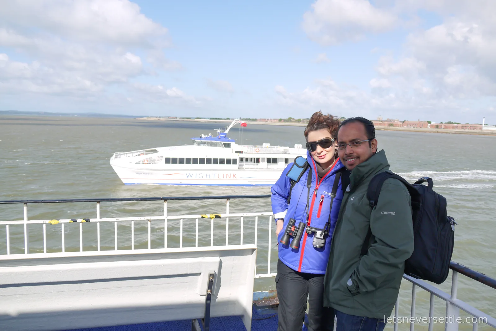 Inga and Dileep on the ferry deck with a white Wightlink fast catamaran crossing the Solent behind them