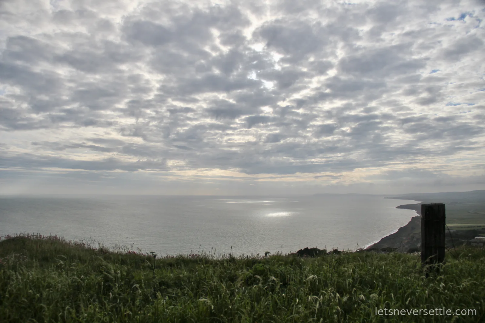 Silver light breaking through a blanket of cloud over the sea and a long curve of coastline