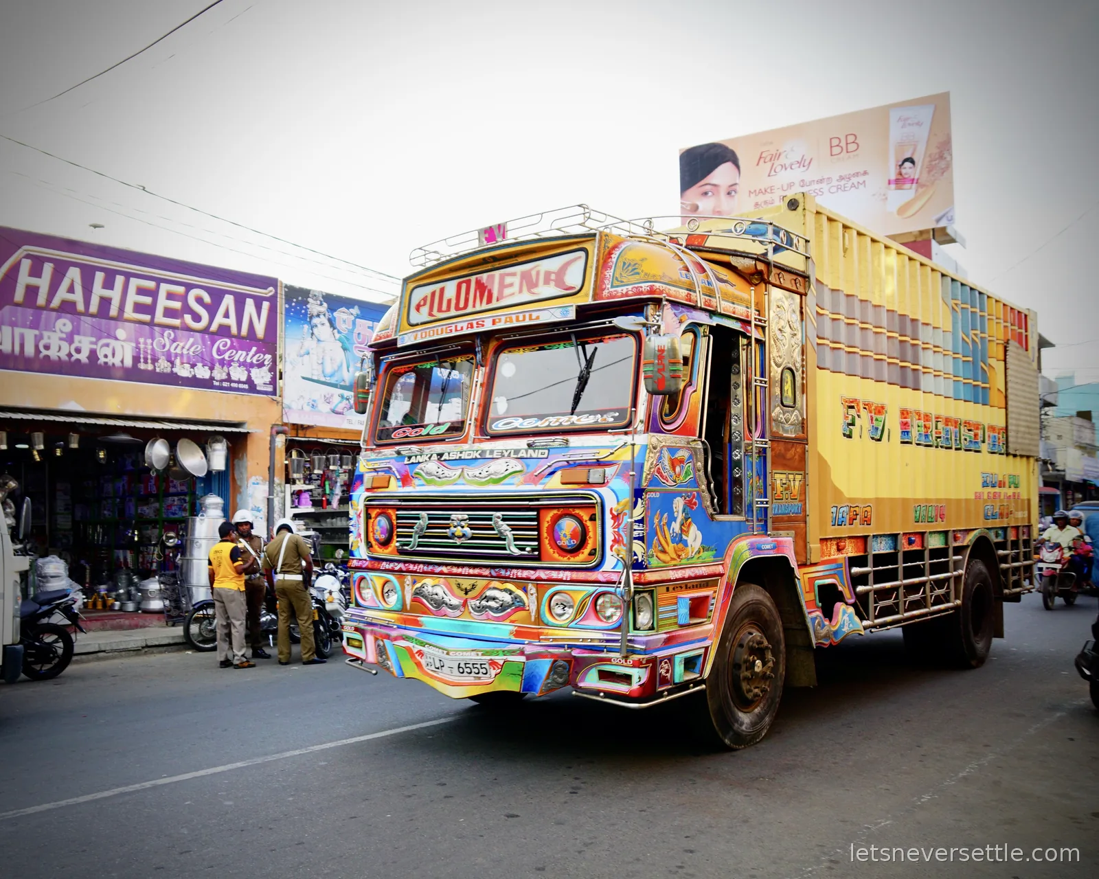 A lorry painted in bright multicoloured patterns with the name Philomena across the top of the cab, driving down a Jaffna street