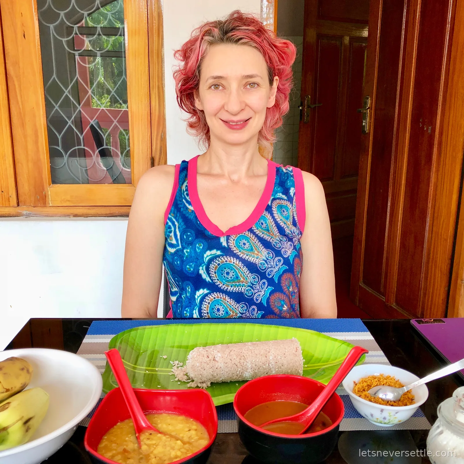Inga at a table with a roll of steamed pittu on a banana leaf, bowls of dhal and curry, coconut sambol and a plate of bananas