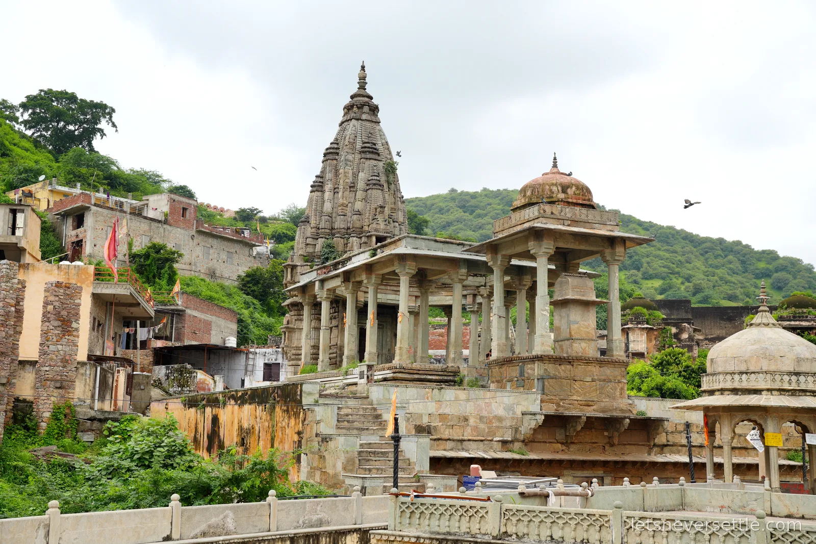 An old stone temple with a carved shikhara tower and dome pavilions on a green hillside in Amer near Jaipur