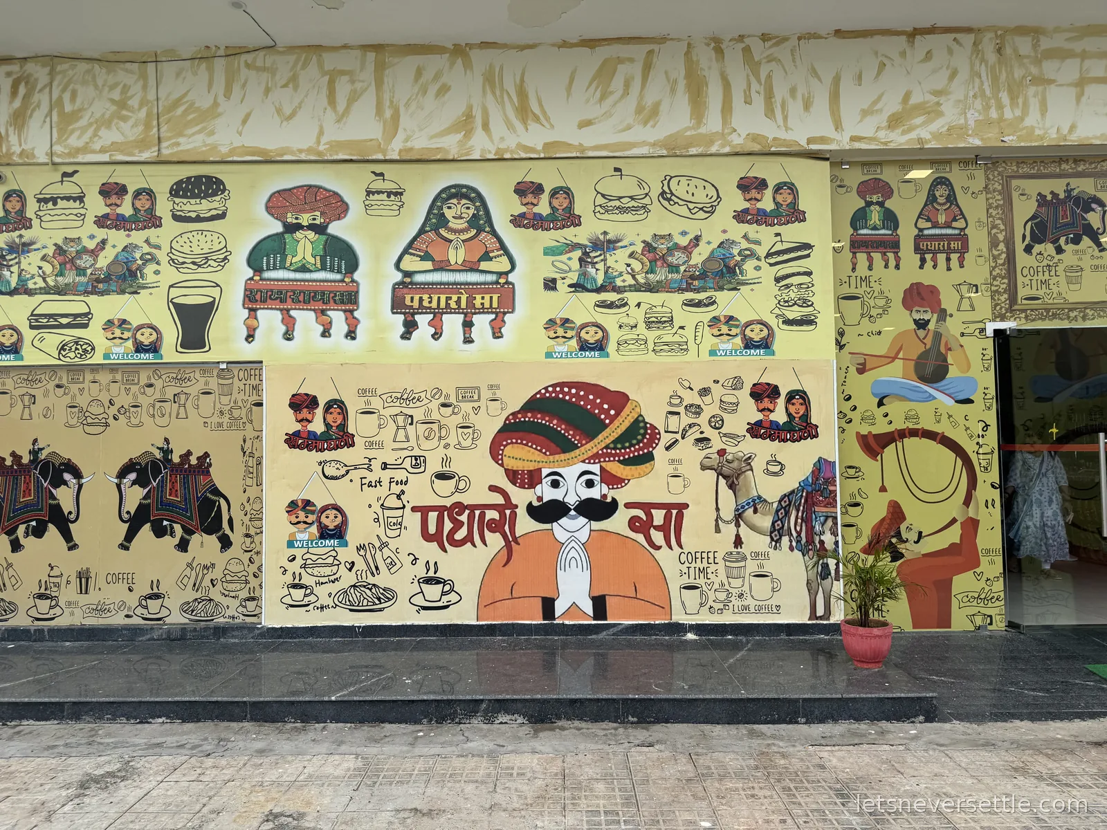 A restaurant facade near Jaipur covered in painted Rajasthani murals of turbaned figures, camels, elephants and the words Padharo Sa