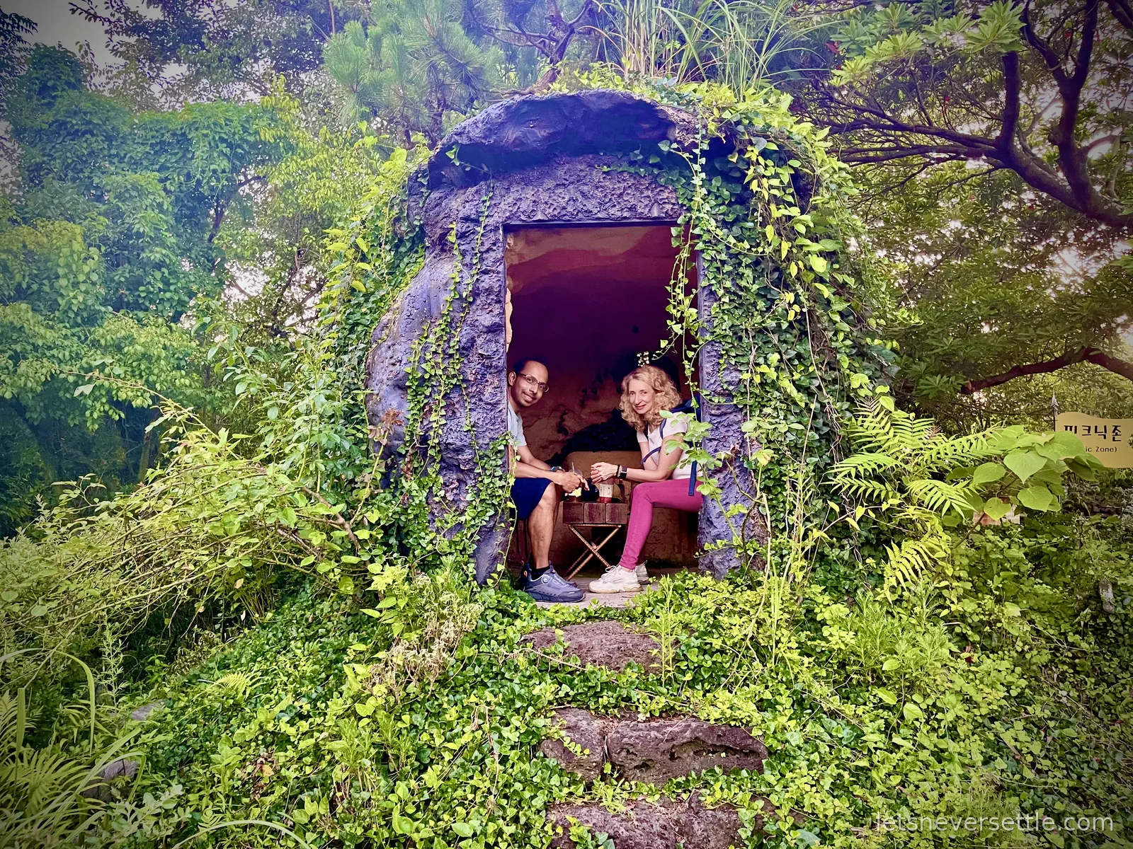 Inga and Dileep sitting inside a small stone dome hut covered in ivy in a lush green garden