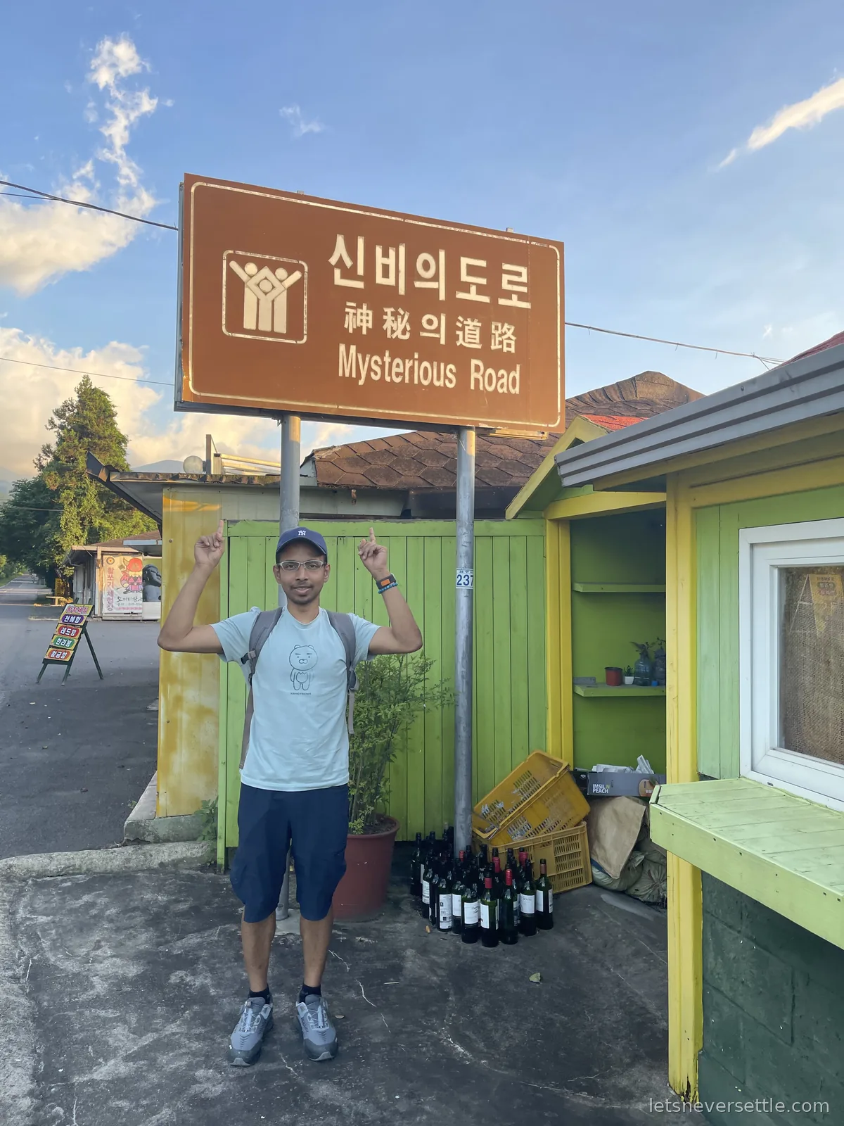 Dileep pointing at the brown Mysterious Road sign written in Korean, Chinese and English on Jeju