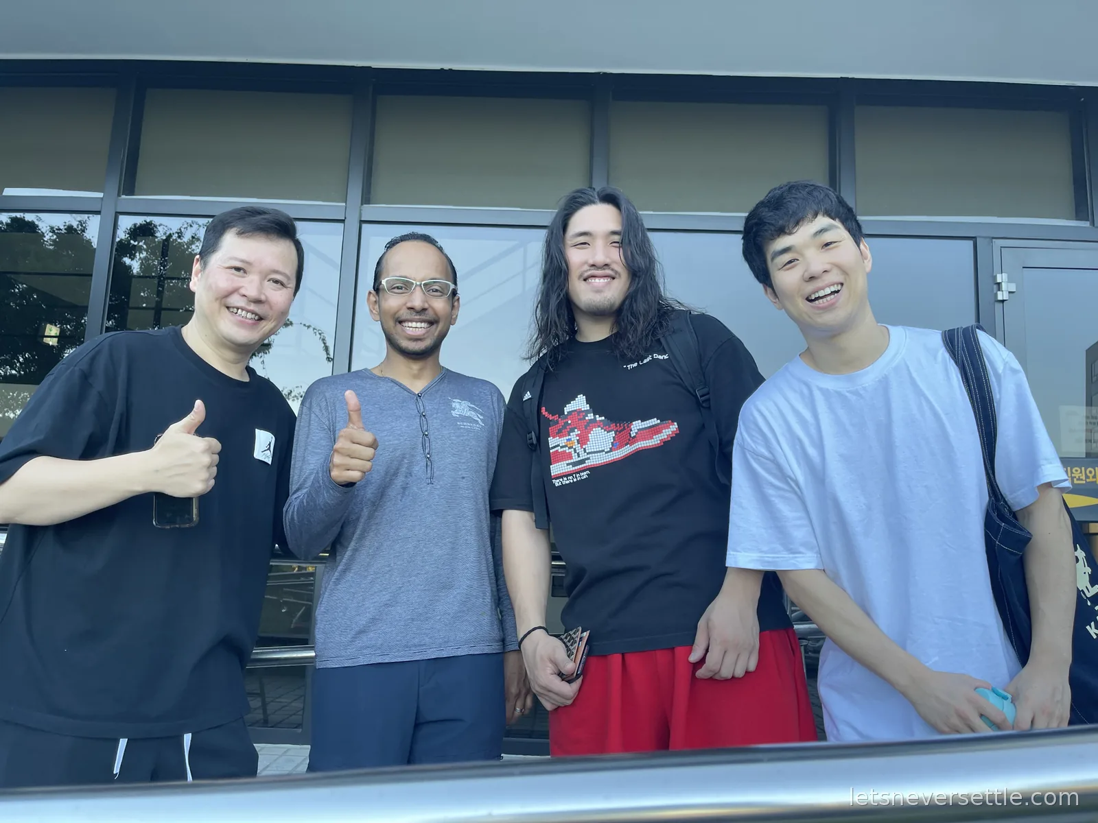Dileep and three new Korean friends grinning with thumbs up outside a glass-fronted building on Jeju
