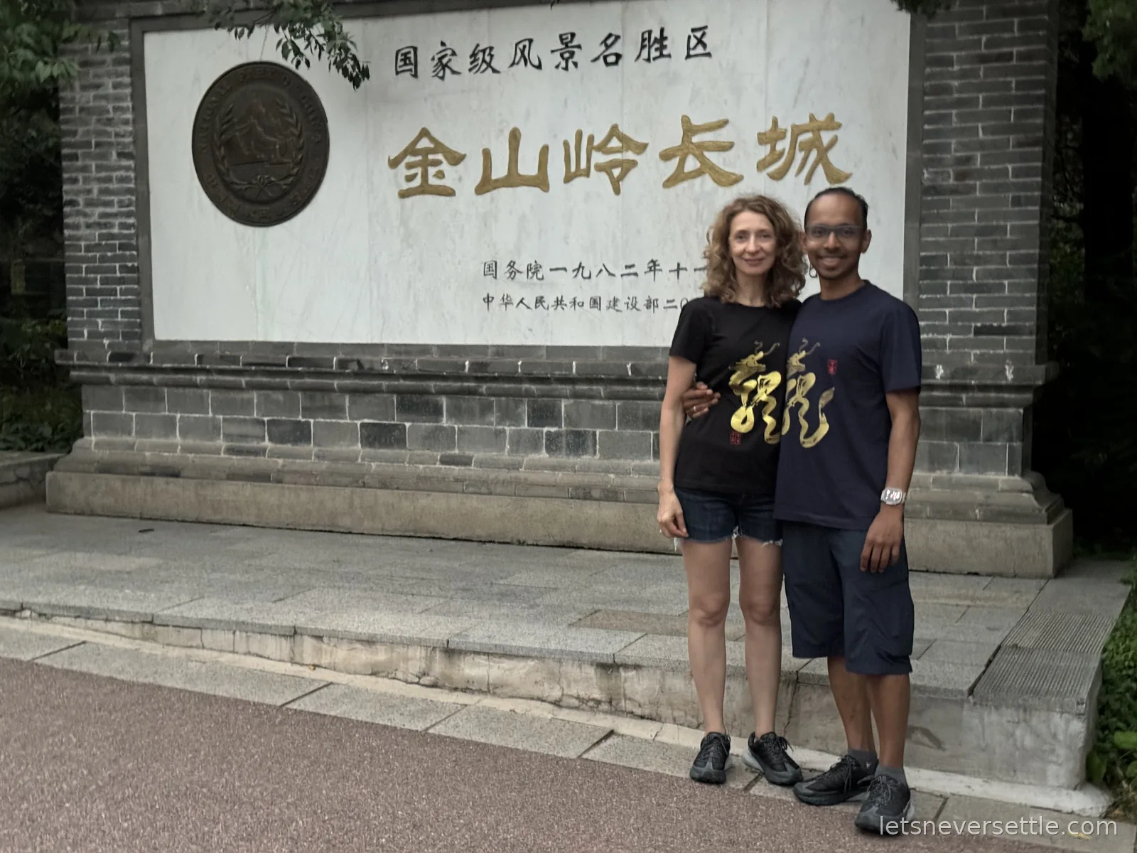 Inga and Dileep in dragon t-shirts in front of the stone entrance monument of the Jinshanling Great Wall scenic area