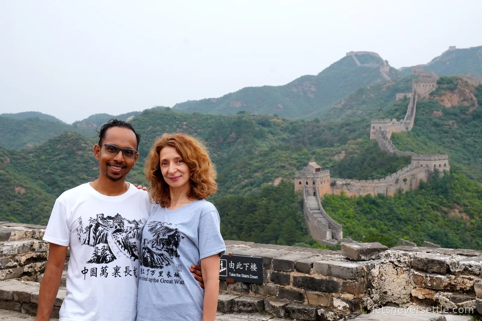 Inga and Dileep on the ramparts with the wall winding down the green valley and up the far ridge behind them