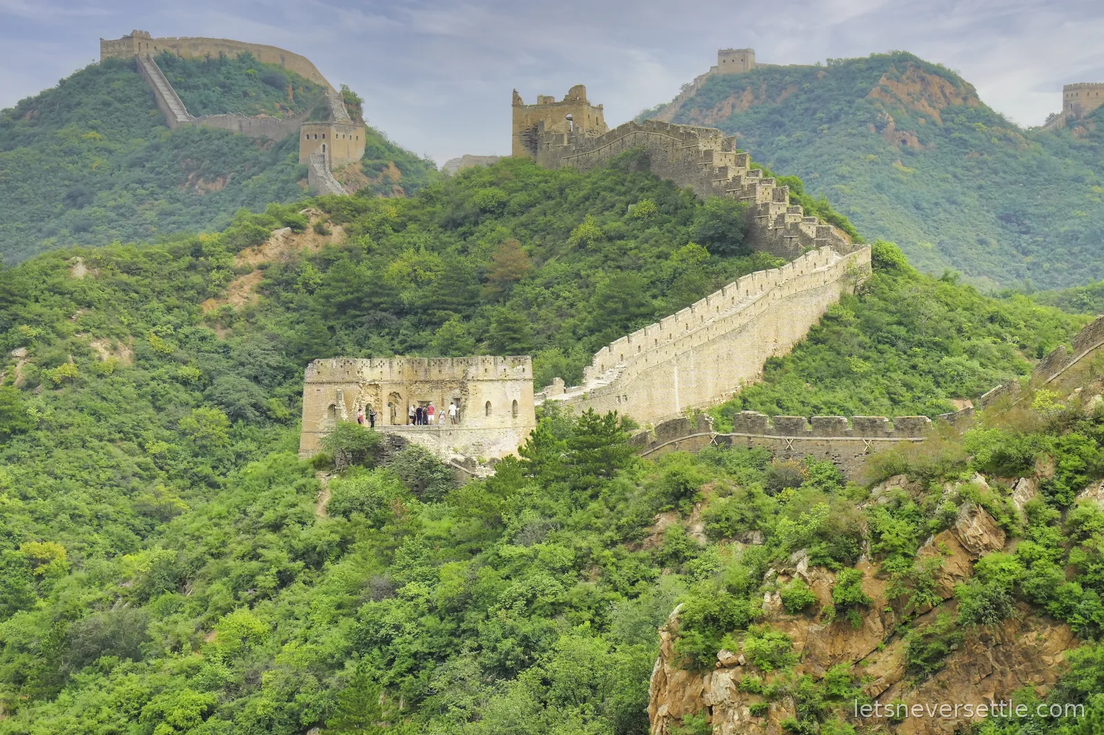 The Jinshanling Great Wall climbing over forested ridges, with ruined and restored watchtowers on every summit
