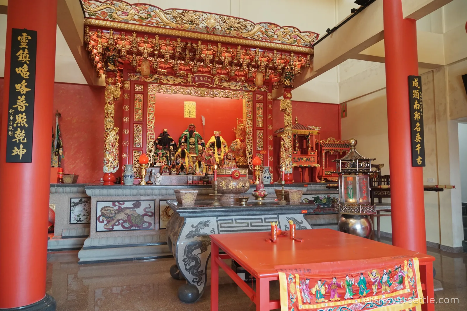 The interior of a Chinese temple in Johor Bahru with red lacquered pillars, gilded carved canopy over the main altar and vertical black calligraphy panels on either side