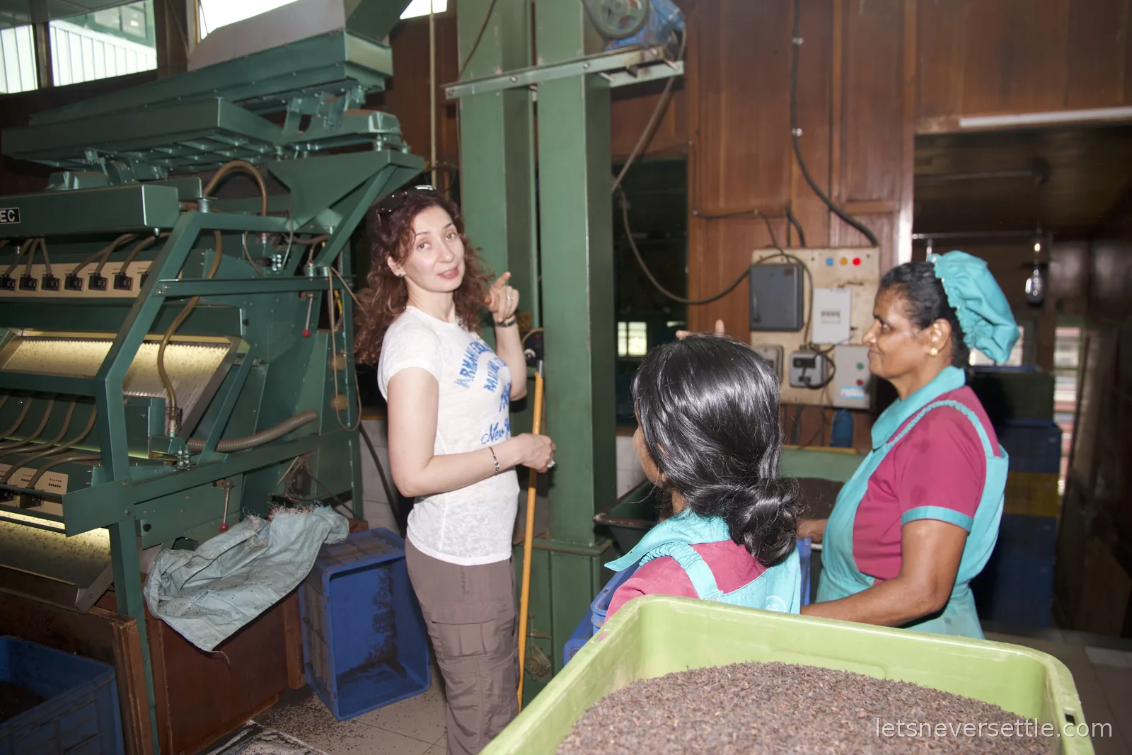 Inga talking with two workers beside a green colour sorting machine, a tray of dark rolled tea in the foreground