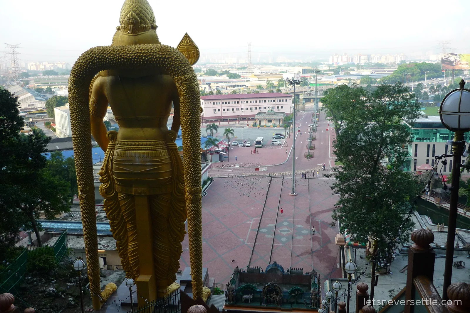 View from the top of the Batu Caves stairs, looking down past the back of the golden statue to the plaza below
