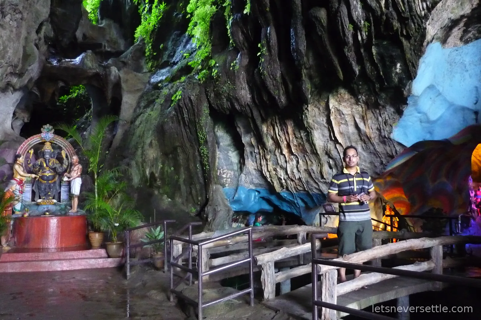 Dileep standing by a shrine and painted statues inside a limestone cavern at Batu Caves