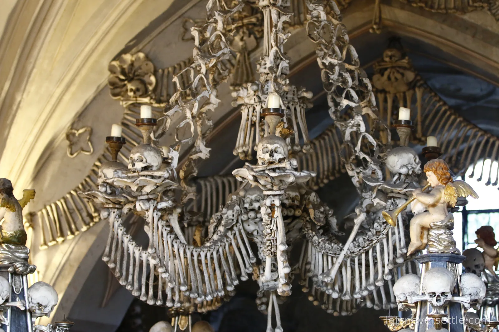 The bone chandelier of the Sedlec Ossuary with skulls holding candles, garlands of bones and a trumpeting cherub beside it