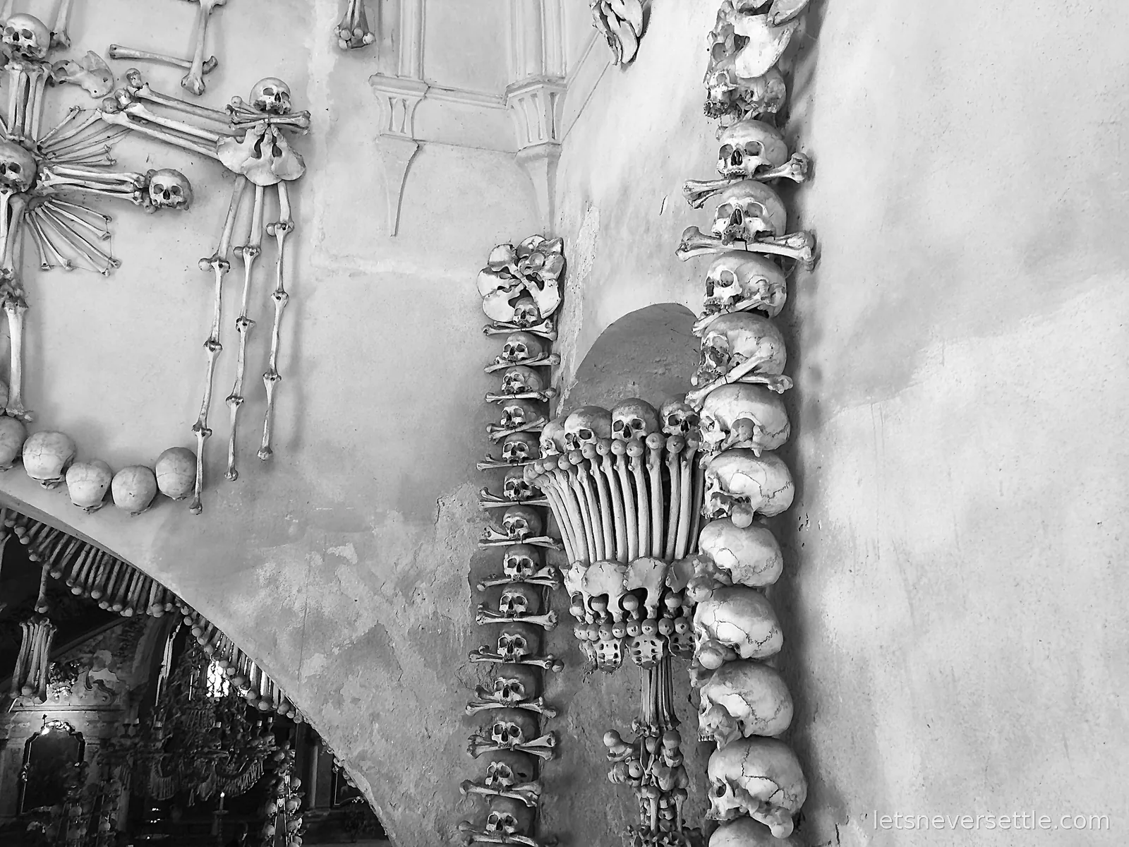 Columns of skulls and crossed bones climbing an archway in the Sedlec Ossuary, with a chalice built of bones between them
