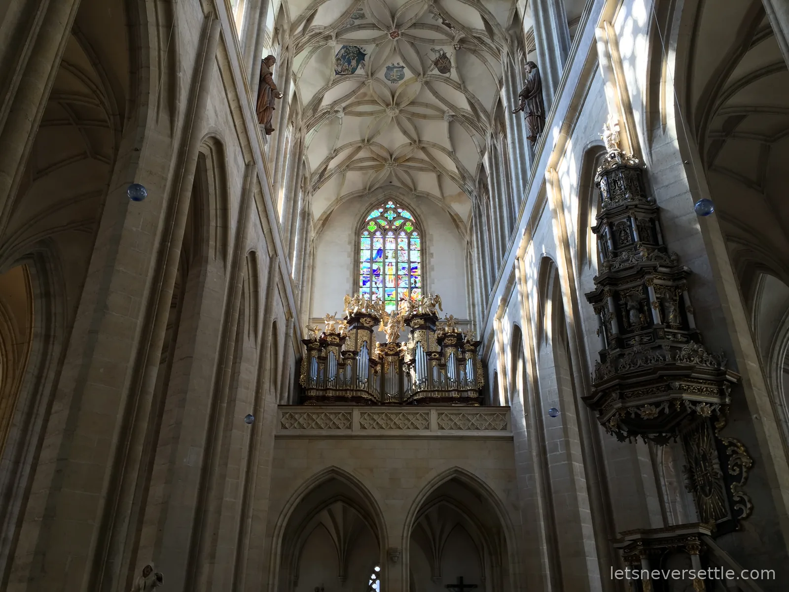 The Gothic nave of St Barbara's Cathedral in Kutna Hora with ribbed vaulting, a stained glass window and an ornate organ loft