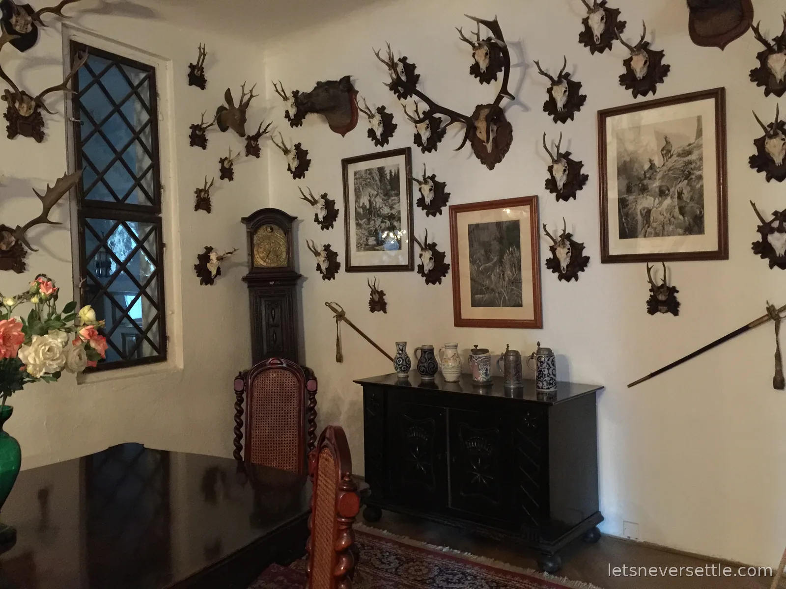 A room in Cesky Sternberk Castle with walls covered in mounted antlers and deer skulls around framed hunting prints and a grandfather clock