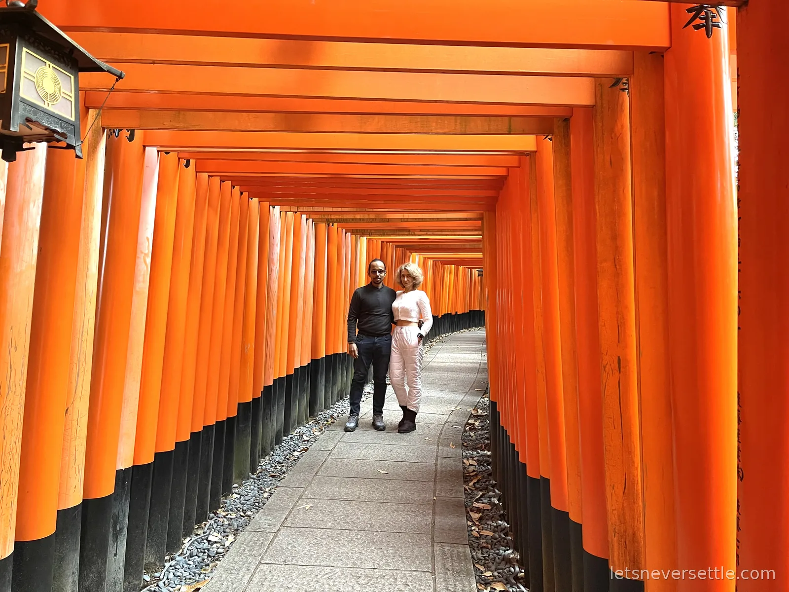 Inga and Dileep walking through a tunnel of closely spaced orange torii gates at Fushimi Inari shrine