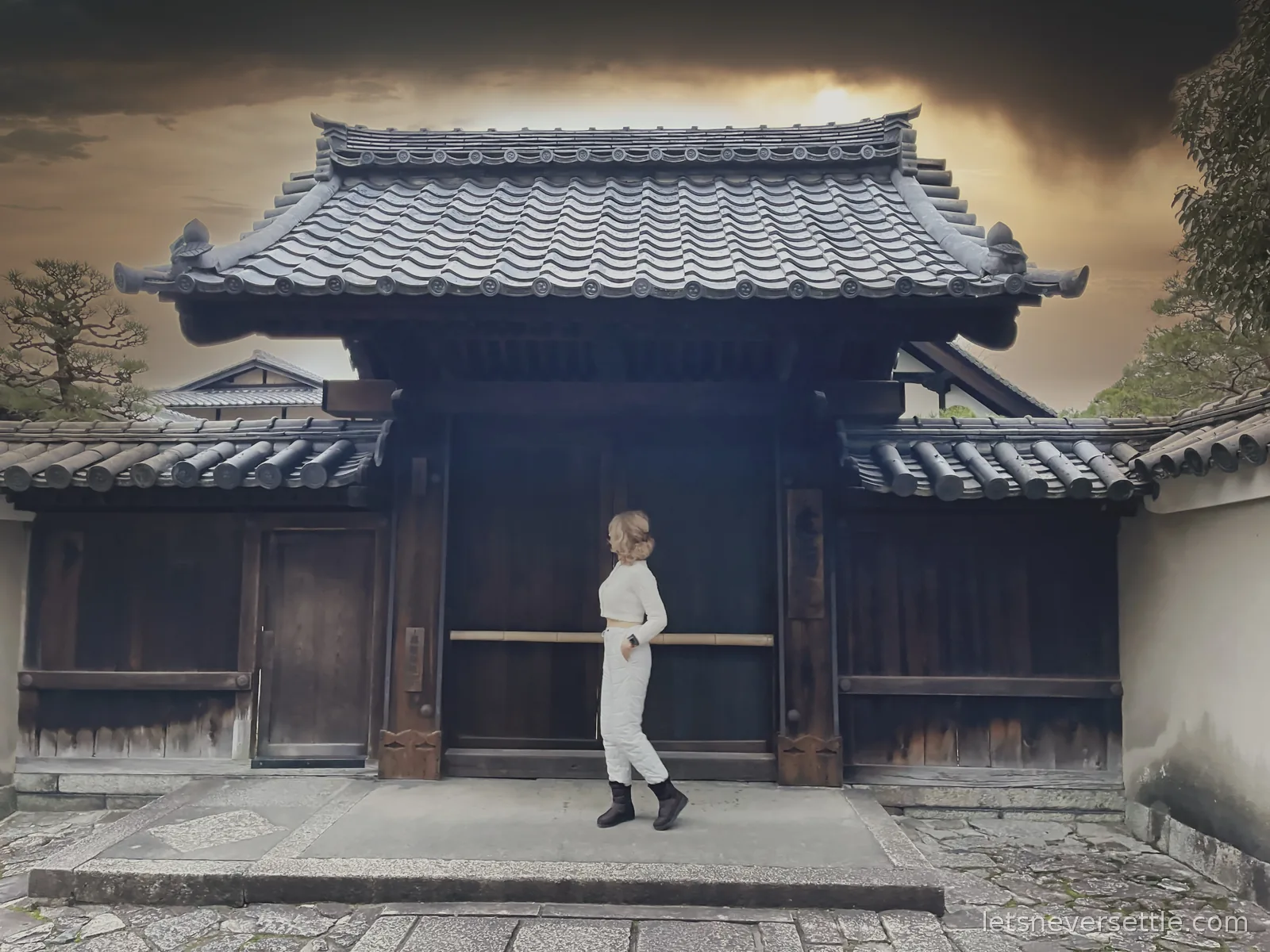 Inga walking past a dark tiled temple gate in Kyoto under a dramatic golden evening sky
