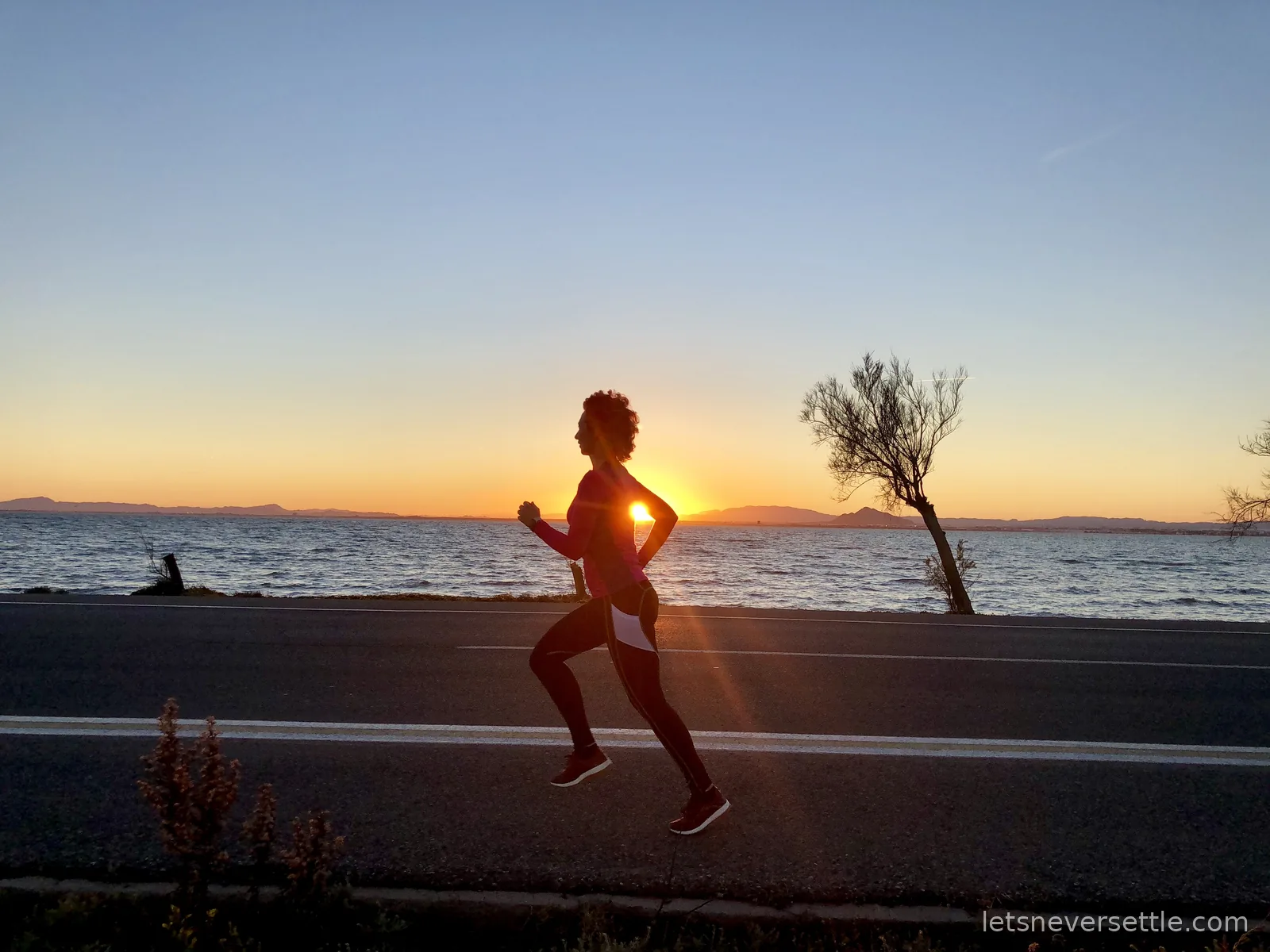Inga running along a coastal road at sunset, the sun dropping behind mountains across the Mar Menor lagoon