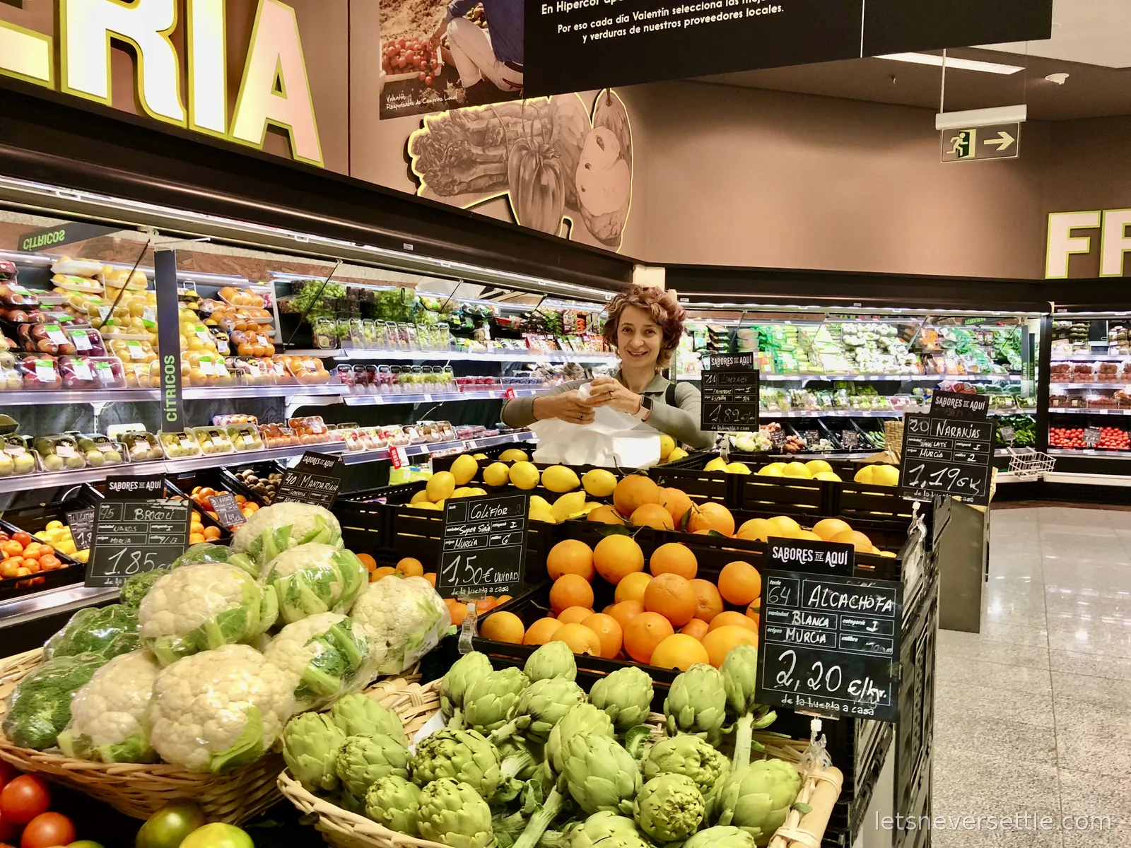 Inga bagging lemons beside crates of oranges, cauliflowers and artichokes in a Murcia supermarket