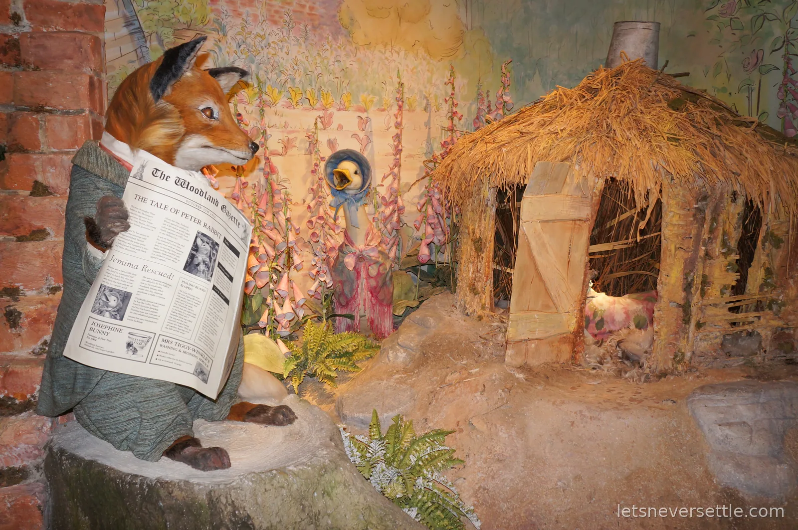 A life-size model of a fox in a tweed jacket reading The Woodland Gazette beside Jemima Puddle-Duck in her bonnet at the World of Beatrix Potter