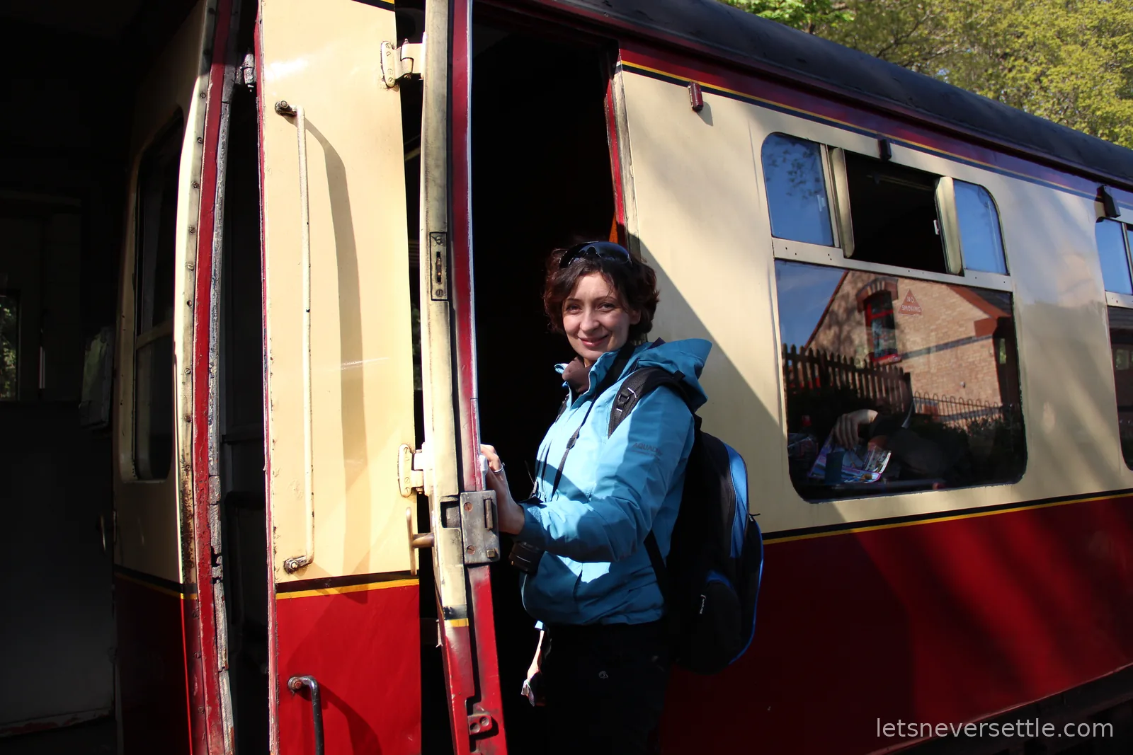 Inga boarding a maroon and cream heritage railway carriage through its wooden door