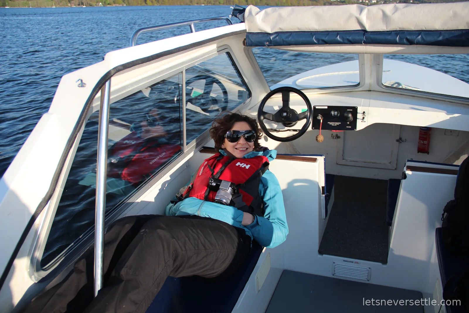 Inga in a red life jacket and sunglasses lounging in the cockpit of a small self-drive motorboat on Windermere