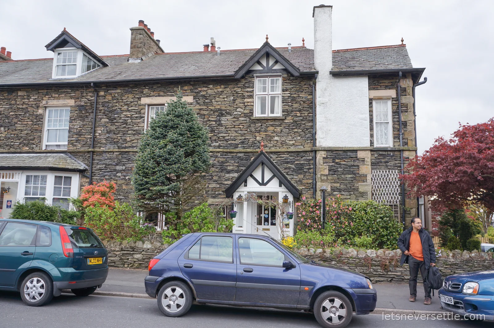 A Victorian stone and slate guesthouse with gabled porch and garden wall, Dileep arriving at the gate with a backpack