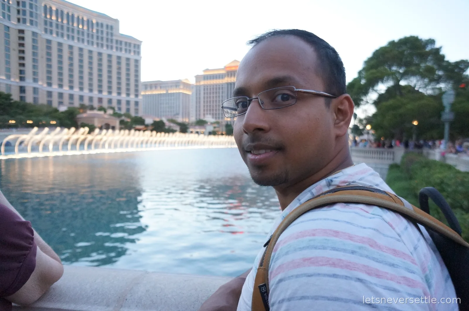 Dileep beside the Bellagio lake with rows of fountain jets firing and Caesars Palace behind