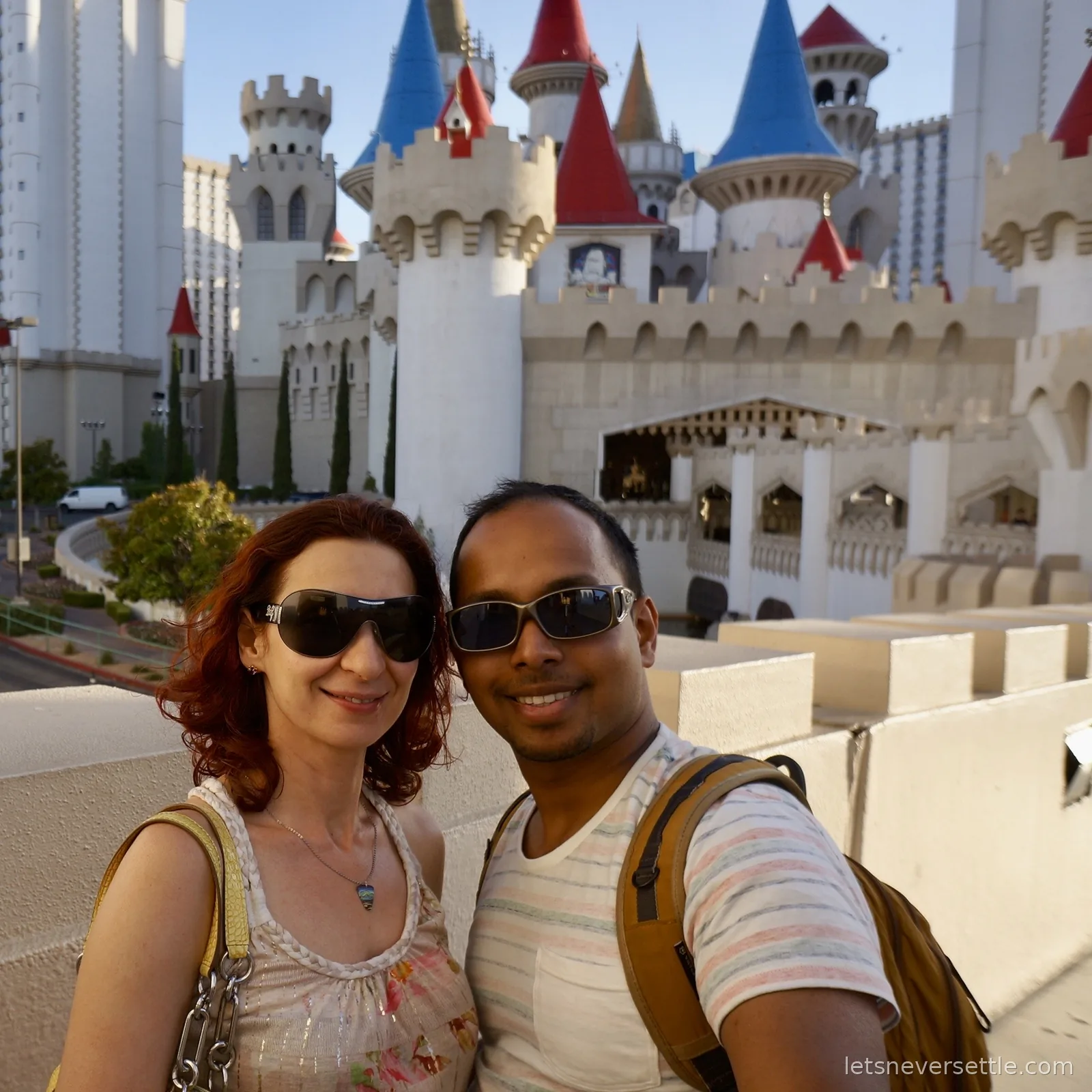 Selfie of Inga and Dileep in sunglasses in front of the white towers and red and blue turrets of the Excalibur castle