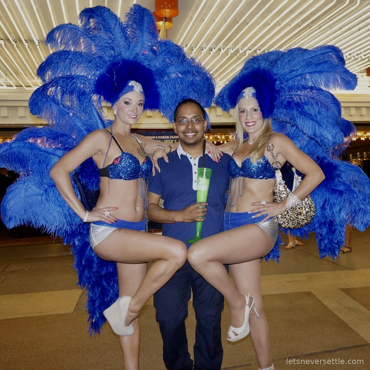 Dileep posing between two showgirls in blue feather headdresses and costumes on Fremont Street