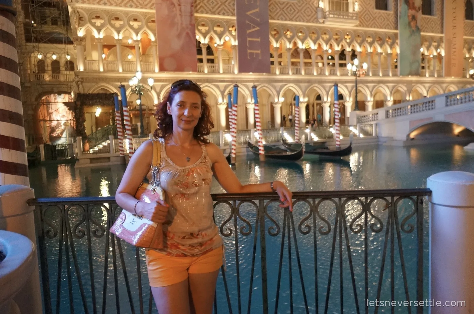 Inga at a railing by the Venetian's outdoor canal at night, gondolas moored at striped poles behind