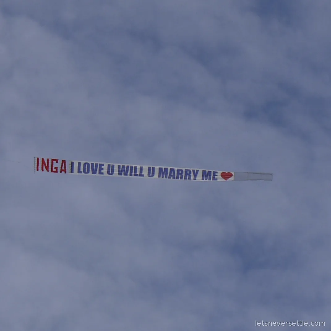 Aerial banner against the clouds reading INGA I LOVE U WILL U MARRY ME with a red heart