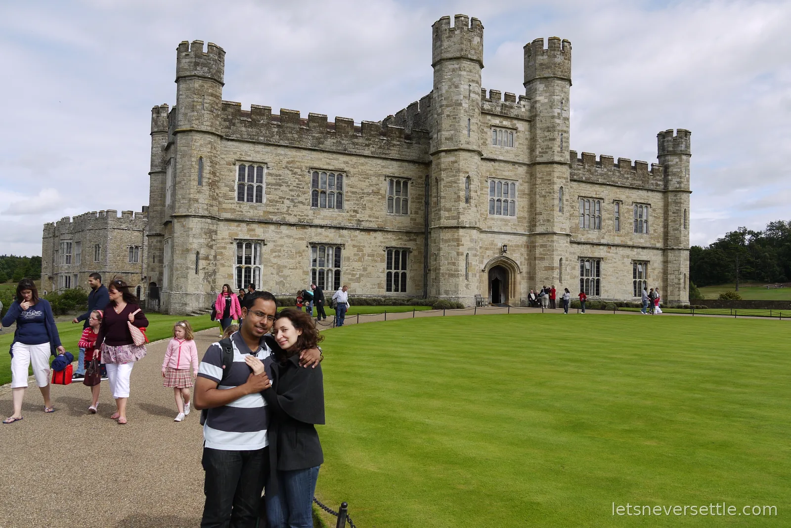 Inga and Dileep embracing on the gravel path in front of the main front of Leeds Castle, newly engaged