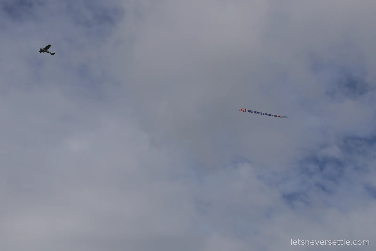 A light aircraft towing the long marriage proposal banner across a cloudy sky above Leeds Castle