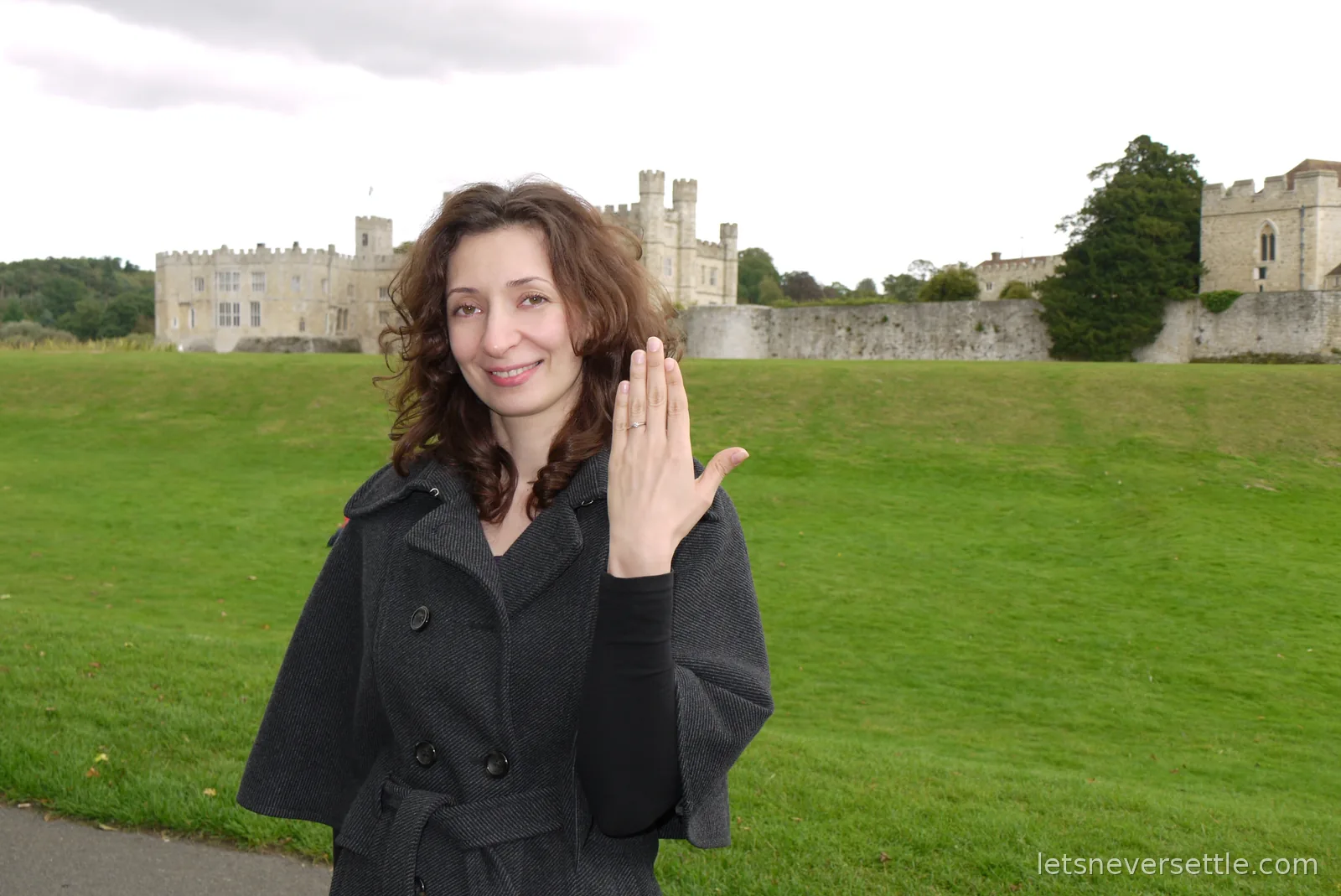 Inga smiling and holding up her hand to show the engagement ring, with Leeds Castle and its walls across the lawn behind her