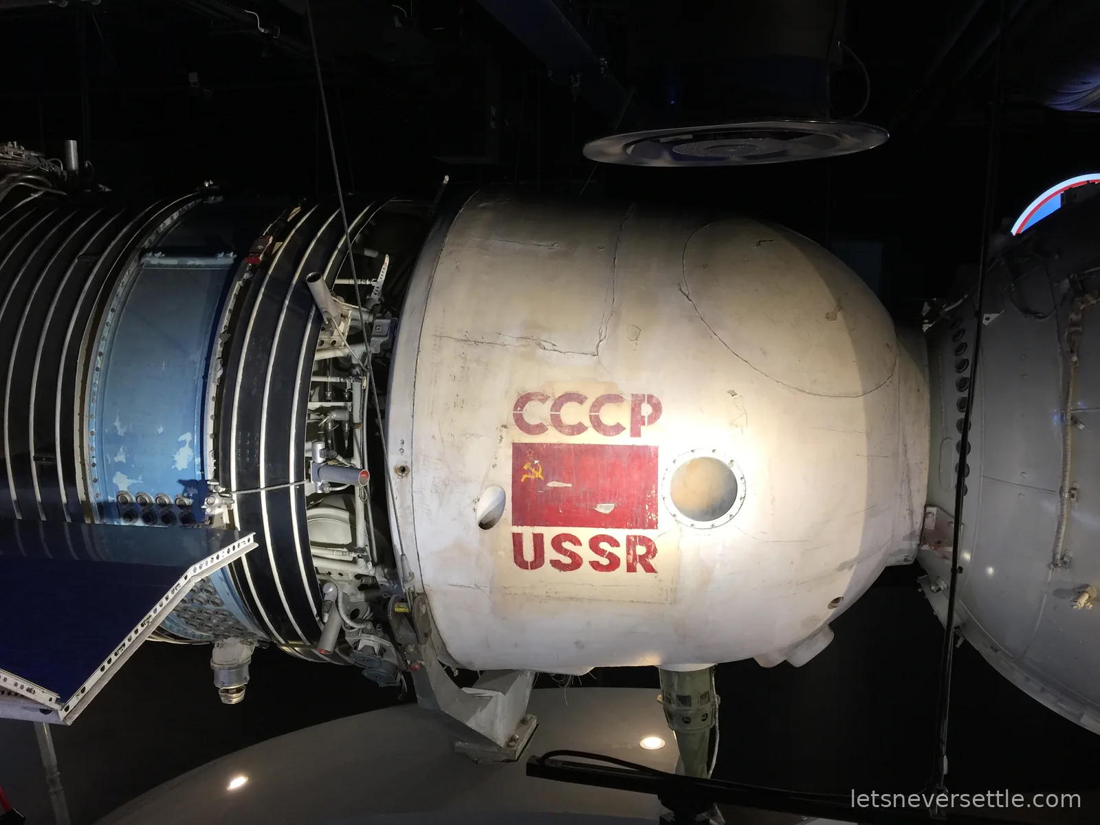 A Soviet spacecraft marked CCCP USSR with a red hammer-and-sickle flag, displayed in a darkened gallery
