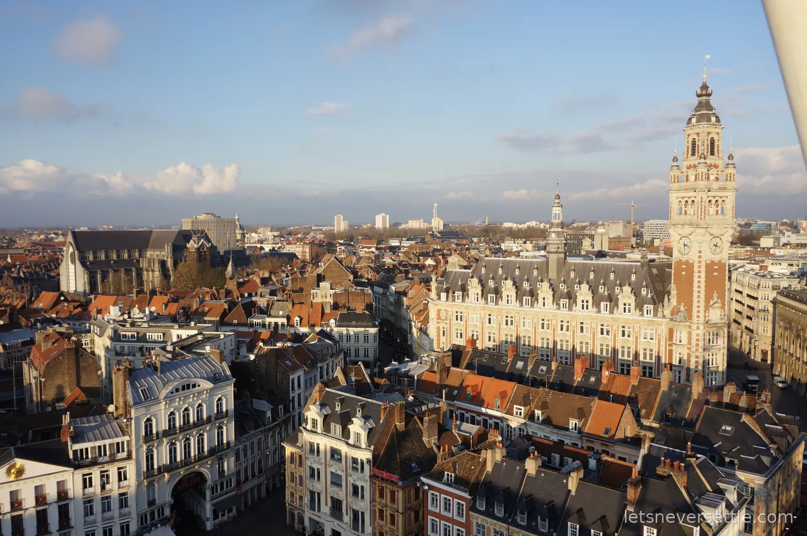 View over the rooftops of Lille old town in low winter sun, with the ornate clock belfry of the Chambre de Commerce on the right