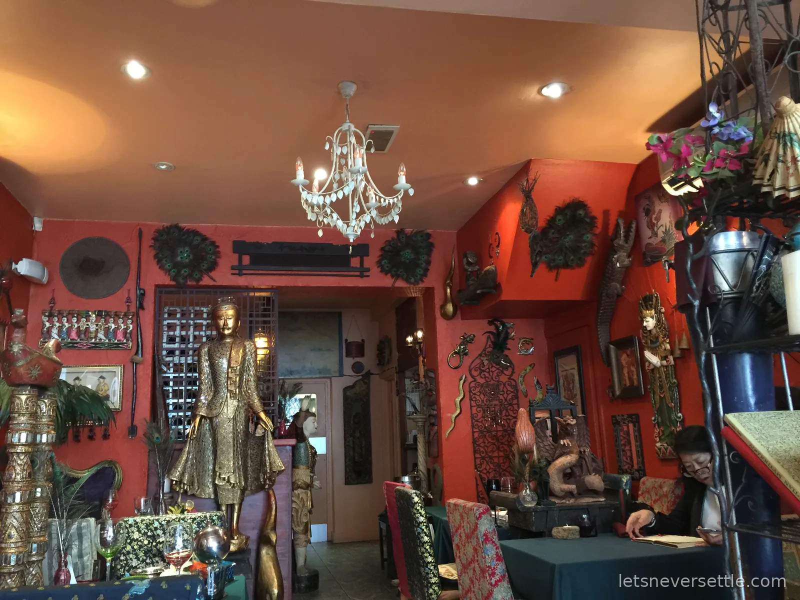 The small red dining room at Archipelago crammed with gilded statues, masks, mirrors and curios above turquoise tablecloths