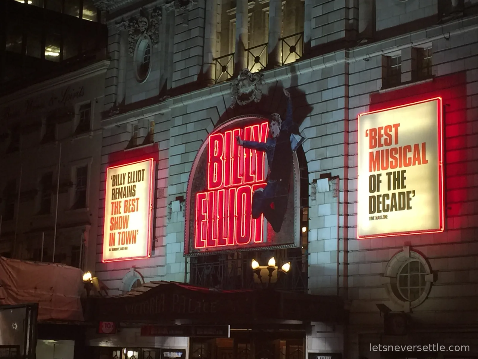 The lit facade of the Victoria Palace Theatre at night showing Billy Elliot The Musical