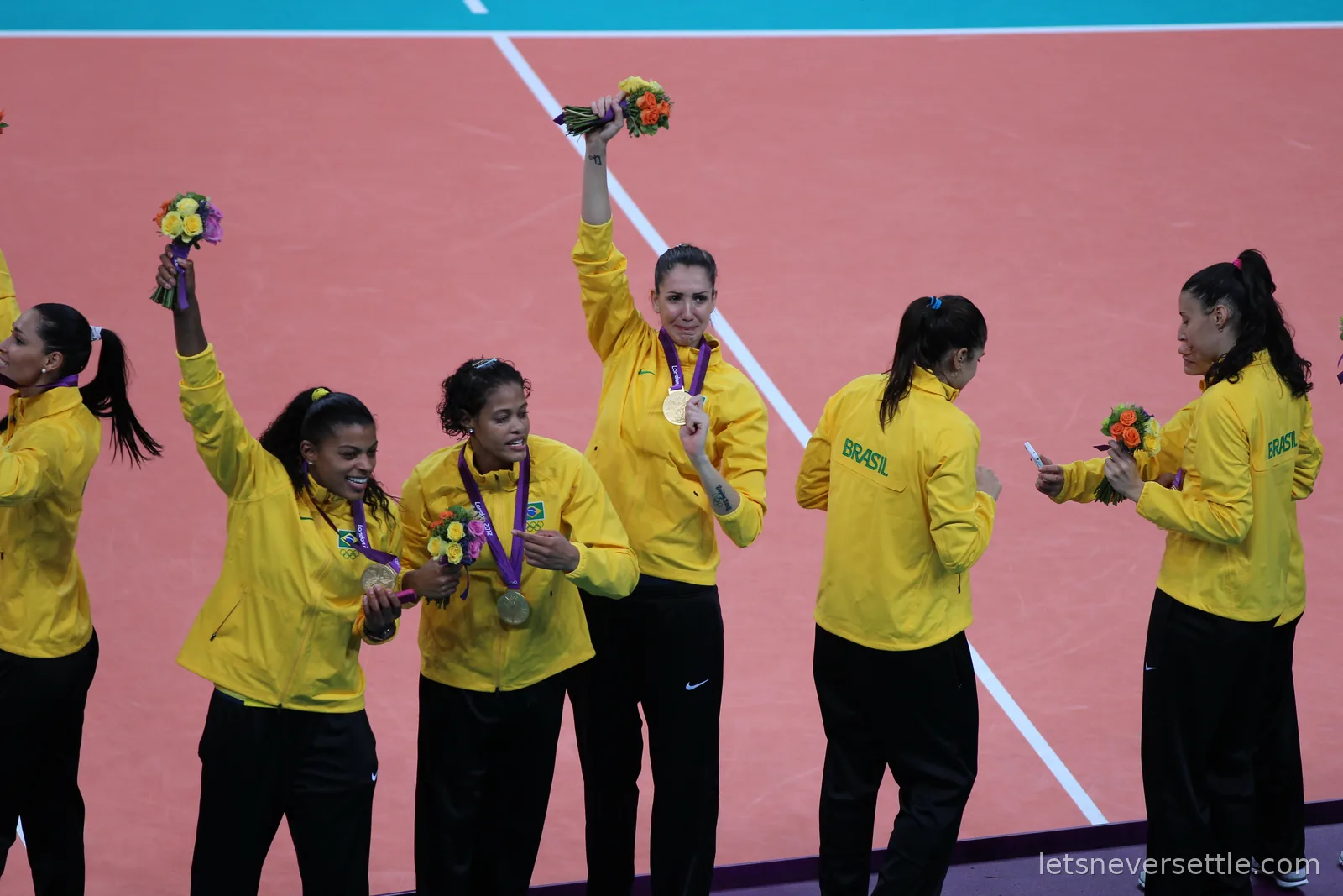 Brazilian players in yellow jackets showing off gold medals and bouquets after the London 2012 women's volleyball final