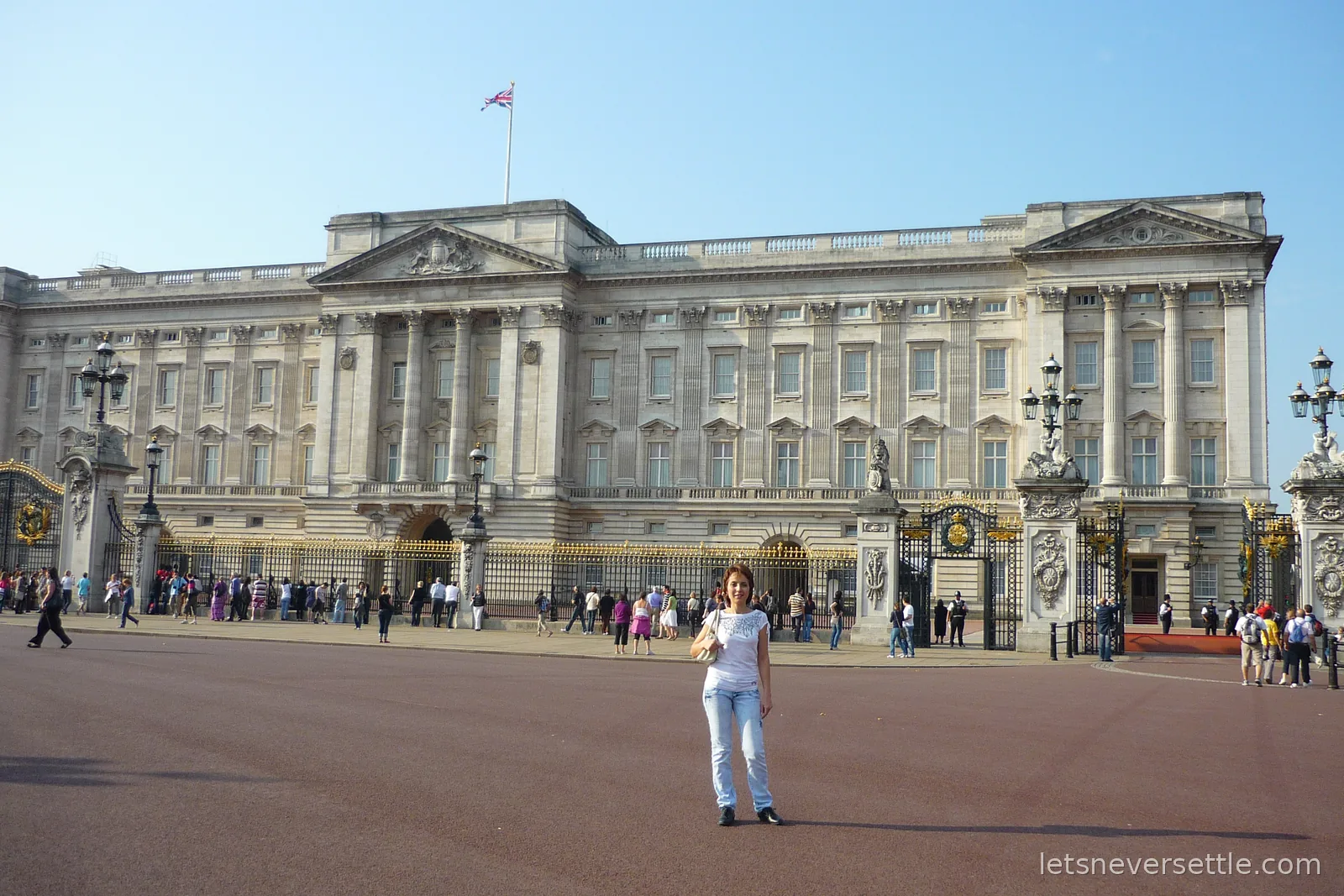 Inga standing on the red tarmac in front of the gates of Buckingham Palace on a sunny day, the Union Jack flying above the roofline