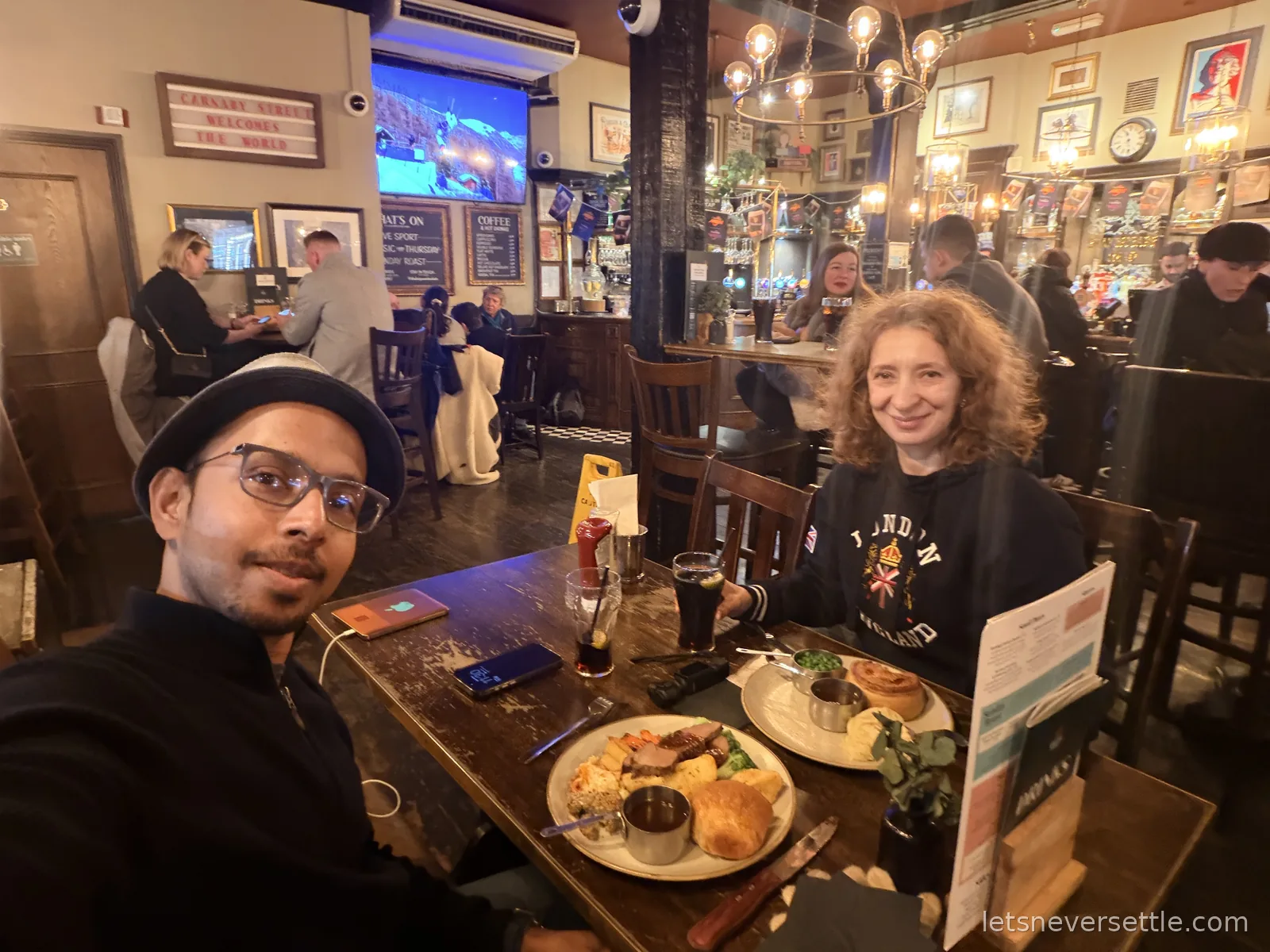 Inga in a London England sweater at a pub table with Sunday roasts, Yorkshire puddings and dark beers, a Carnaby Street sign behind