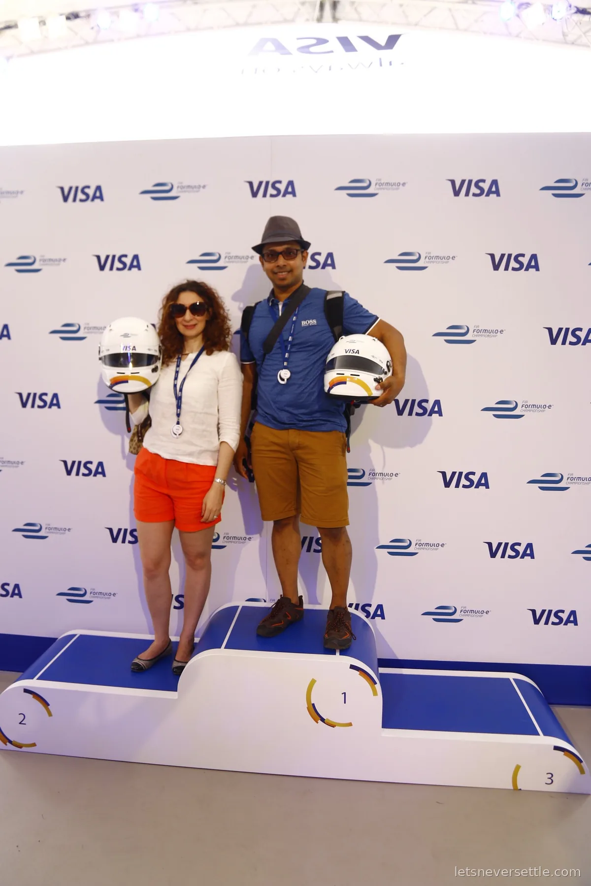 Inga and Dileep posing with race helmets on a fan podium in front of a Formula E and Visa branded wall