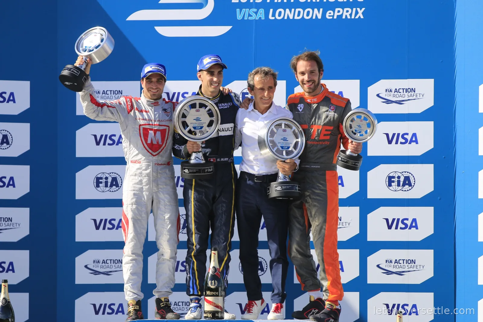 Four men lifting trophies on a podium under a banner reading 2015 FIA Formula E Visa London ePrix