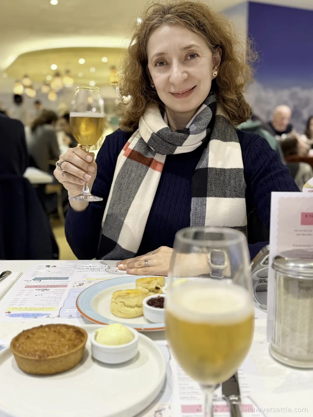 Inga raising a glass over a table of scones, jam and a treacle tart in the Fortnum and Mason tea salon