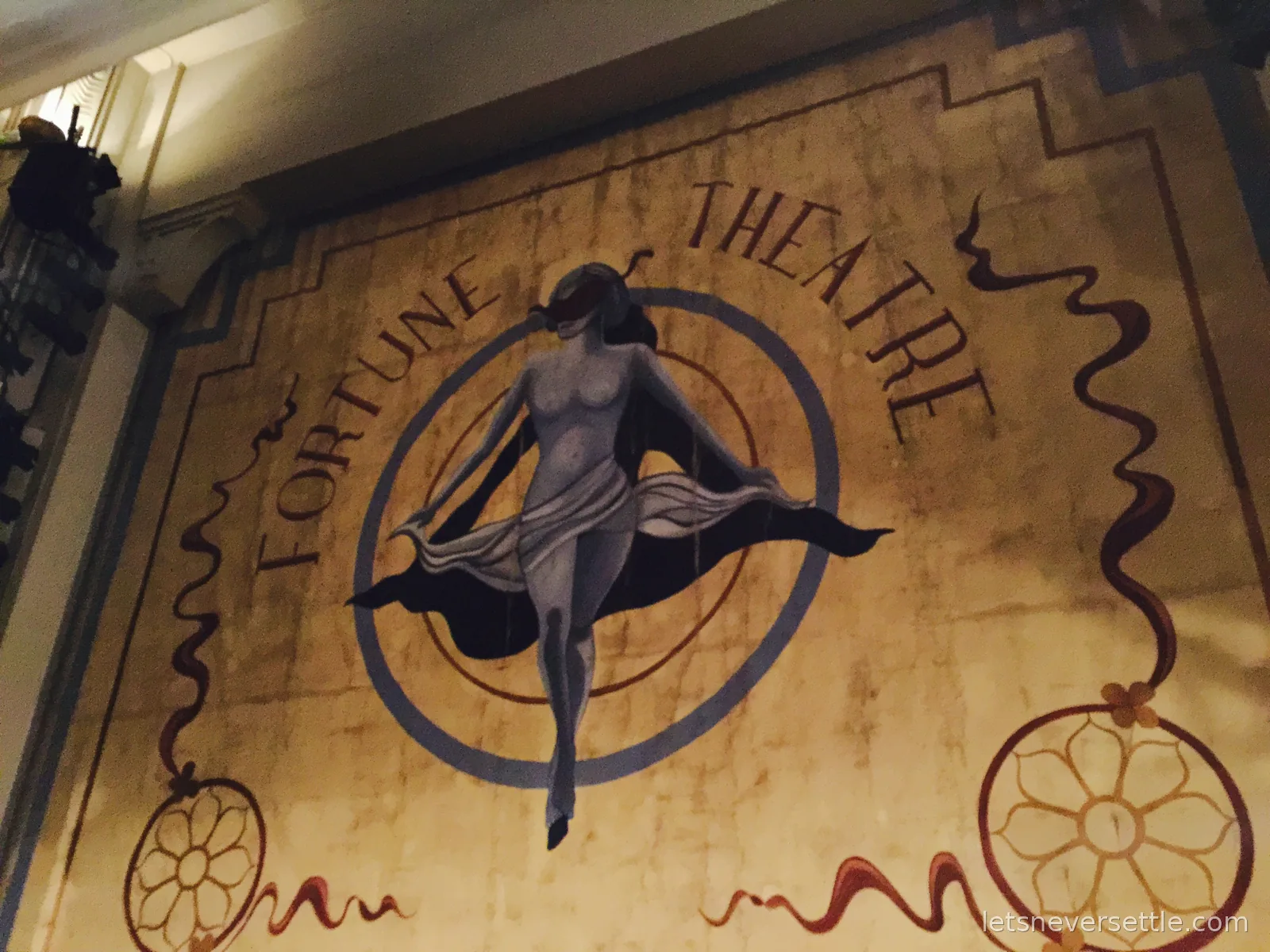 The painted art deco sign of the Fortune Theatre showing a dancing figure inside a circle above the entrance at night