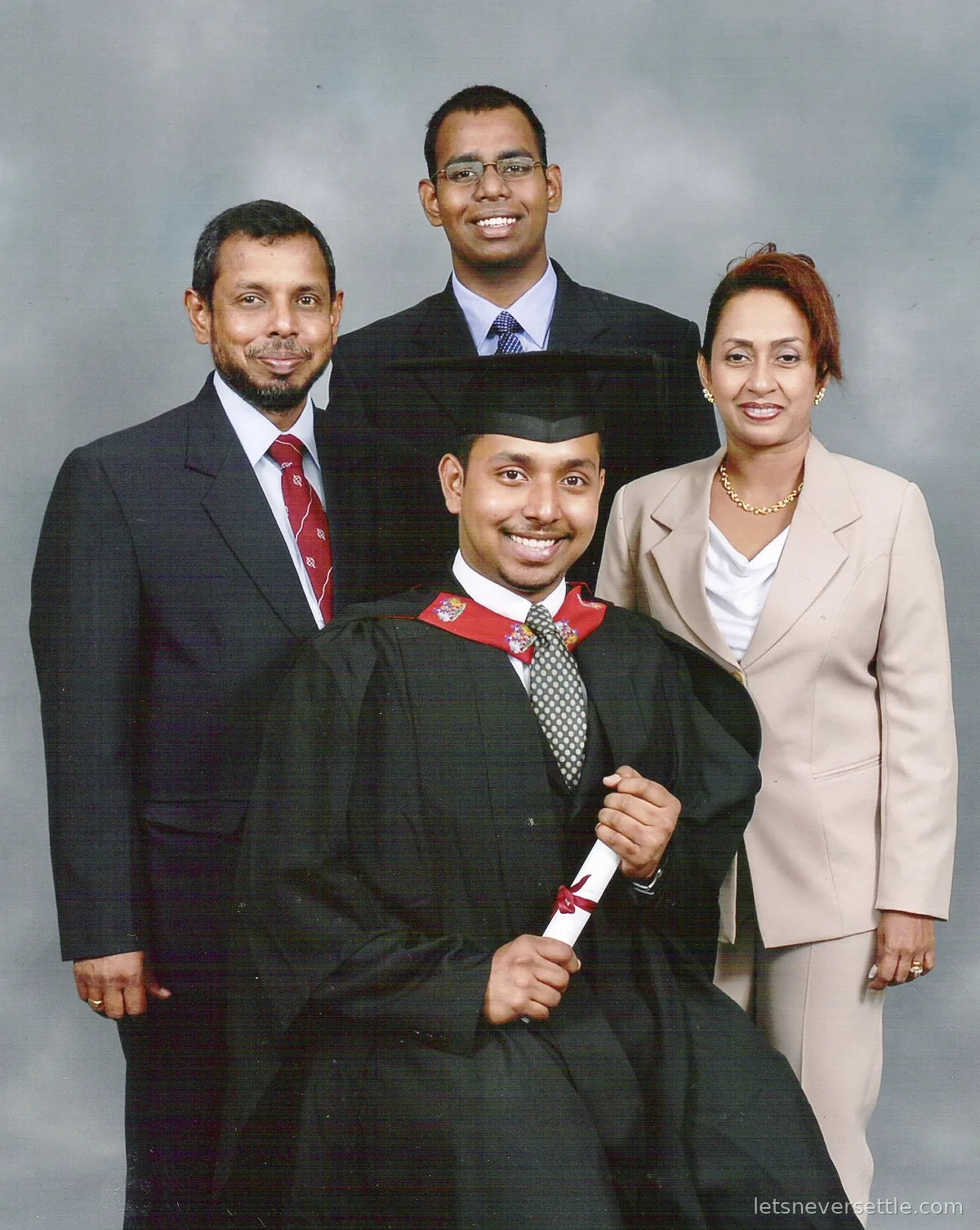 Dileep in graduation gown and mortarboard holding his scroll, posing with his mother, father and brother for a studio portrait